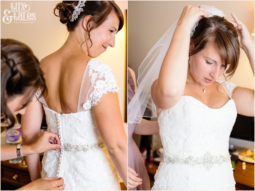 Bride putting on veil in UK wearing a dress with lace a beading detail photographed using side window light