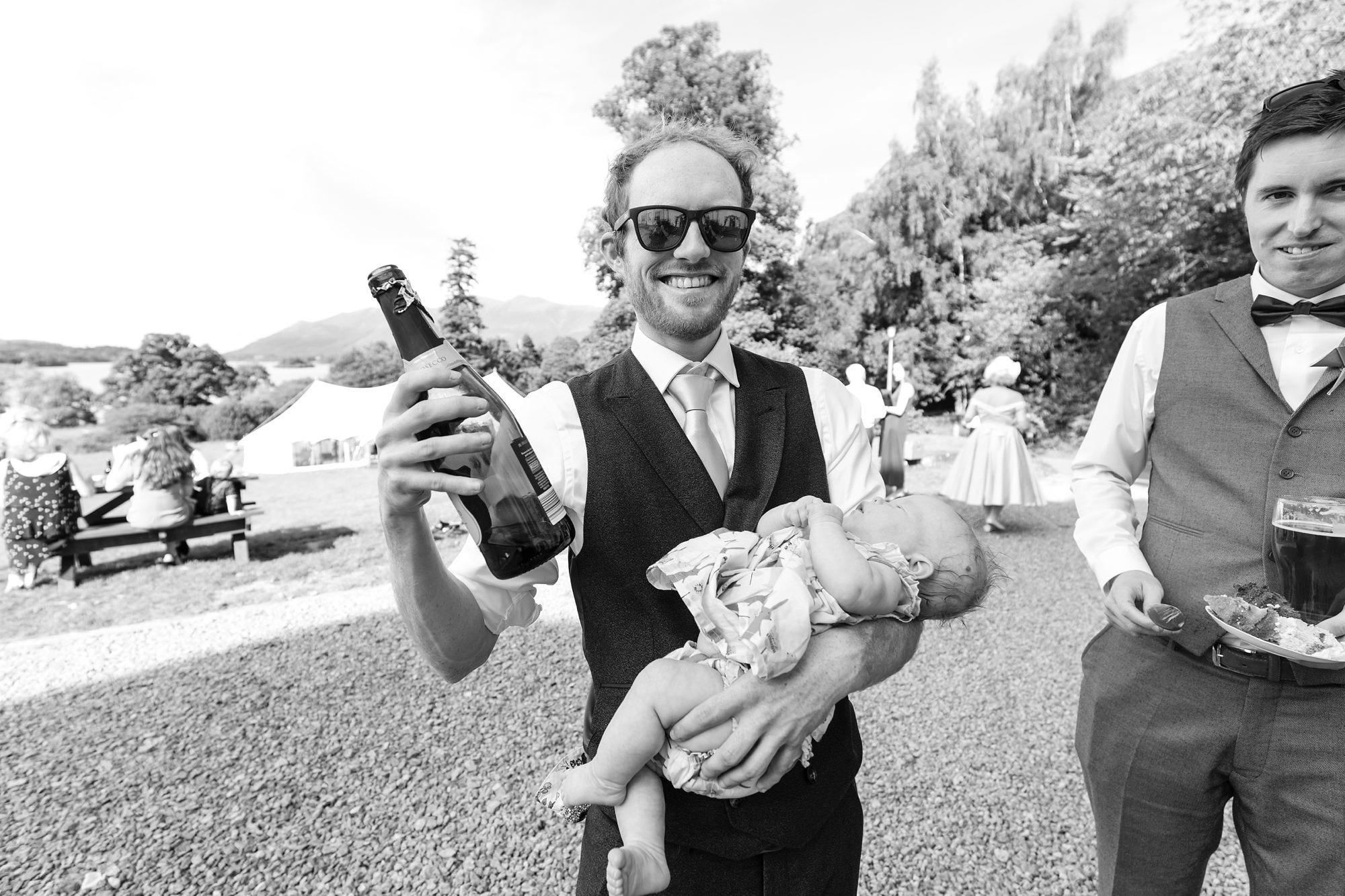 Dad holds baby and has a beer in other hand Derwentwater Independent Hostel Wedding
