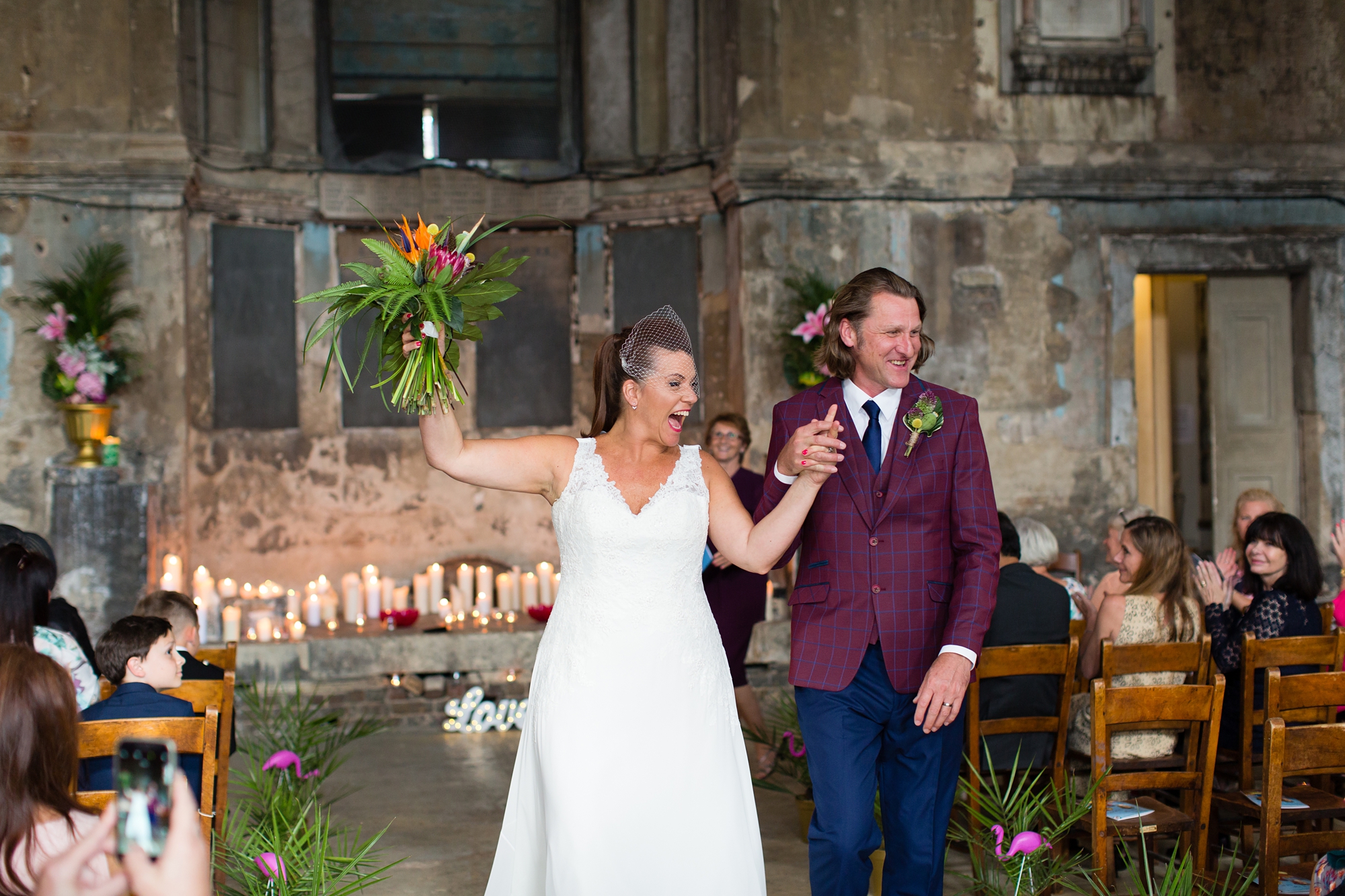 Bride and groom cheer as they walk up the aisle at quirky & fun wedding in London Asylum 