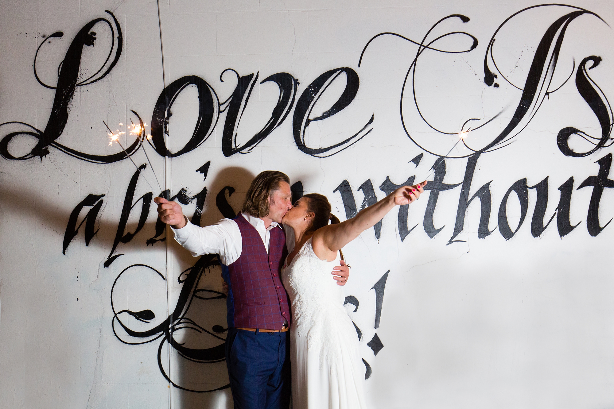 Bride and groom hold up sparklers at London wedding in front of graffiti
