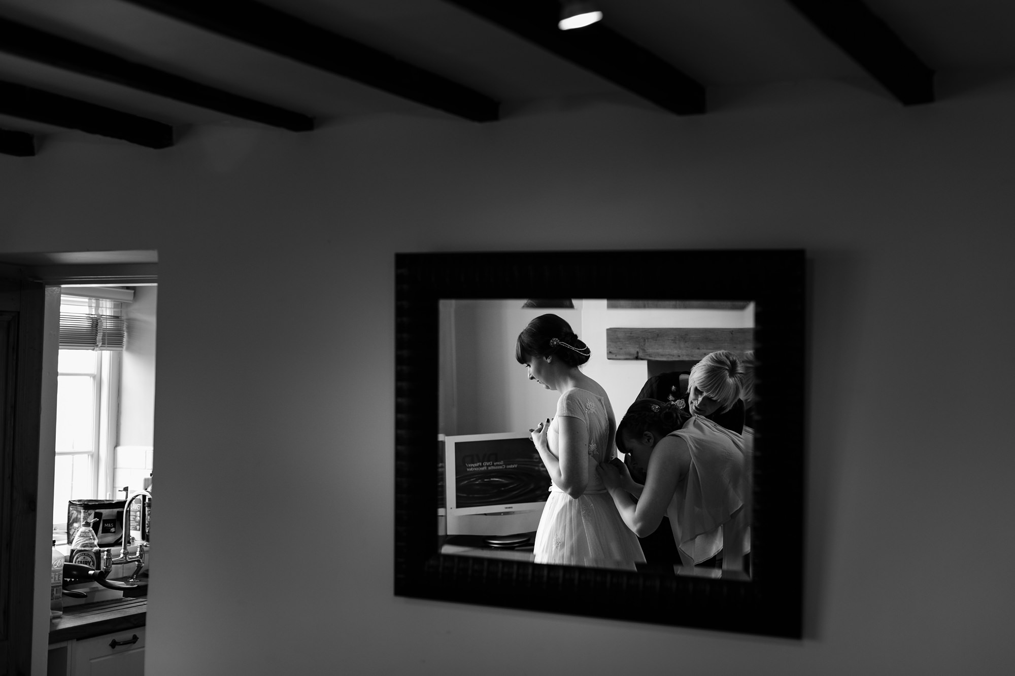 Bridesmaids buttoning up bride into her wedding dress 
