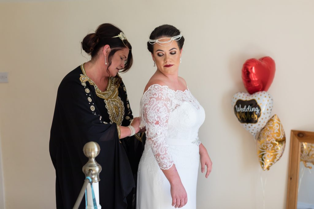 Bride's mother helps her into her dress in a Peaky Blinders themed wedding at Sandurn Hall. 